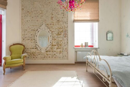 Elegant vintage bedroom featuring a brick wall, ornate mirror, and colorful chandelier.